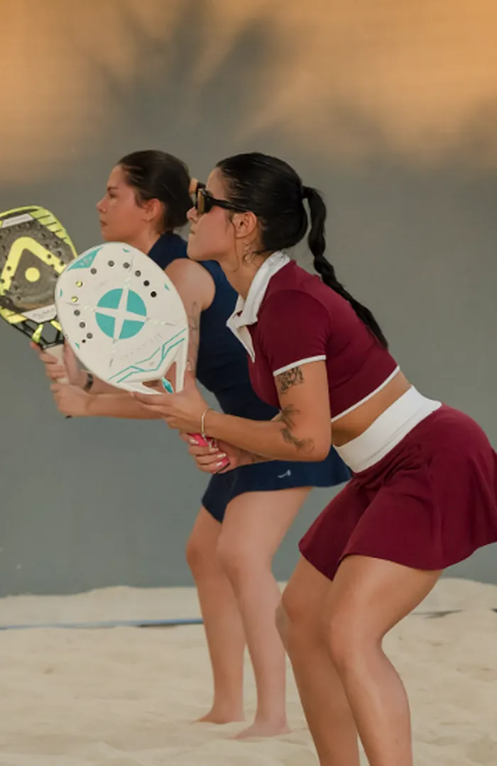 Dupla feminina de beach tennis em posição de espera, raquetes à frente do corpo.