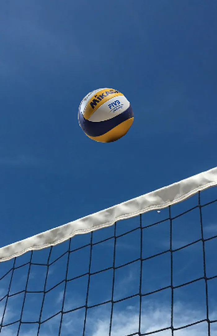 Bola de vôlei suspensa acima da fita branca da rede, contra o céu.